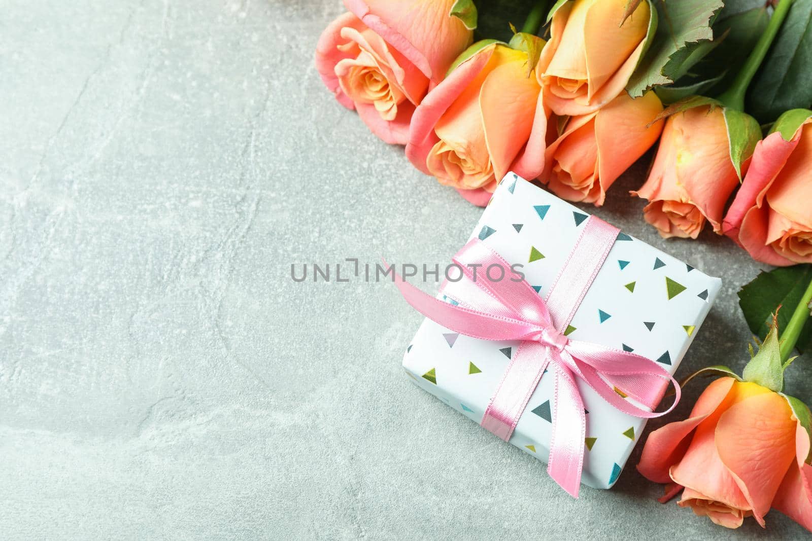 Fresh orange roses with gift and space for text on grey background, closeup by AtlasCompany