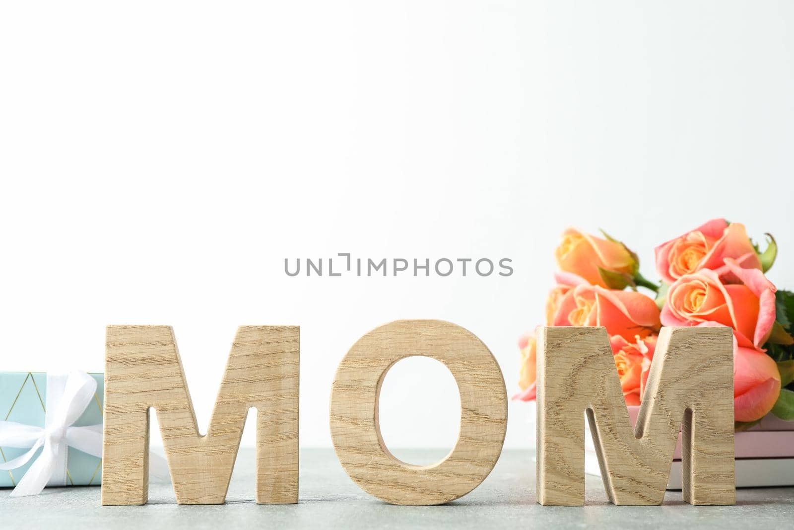 Inscription Mom, beautiful pink roses and gift on grey table against white background, space for text