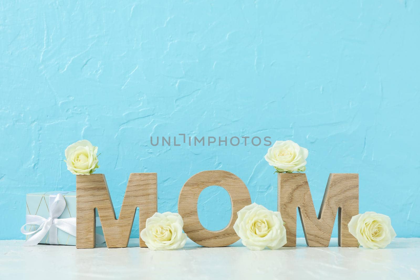 Inscription Mom with white roses on pink table against color background, space for text