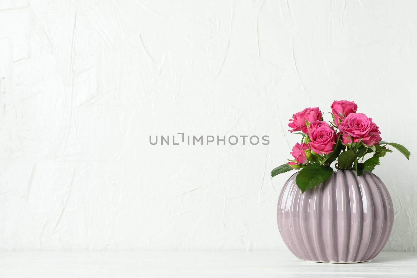 Vase with pink roses and space for text on white table against light background by AtlasCompany