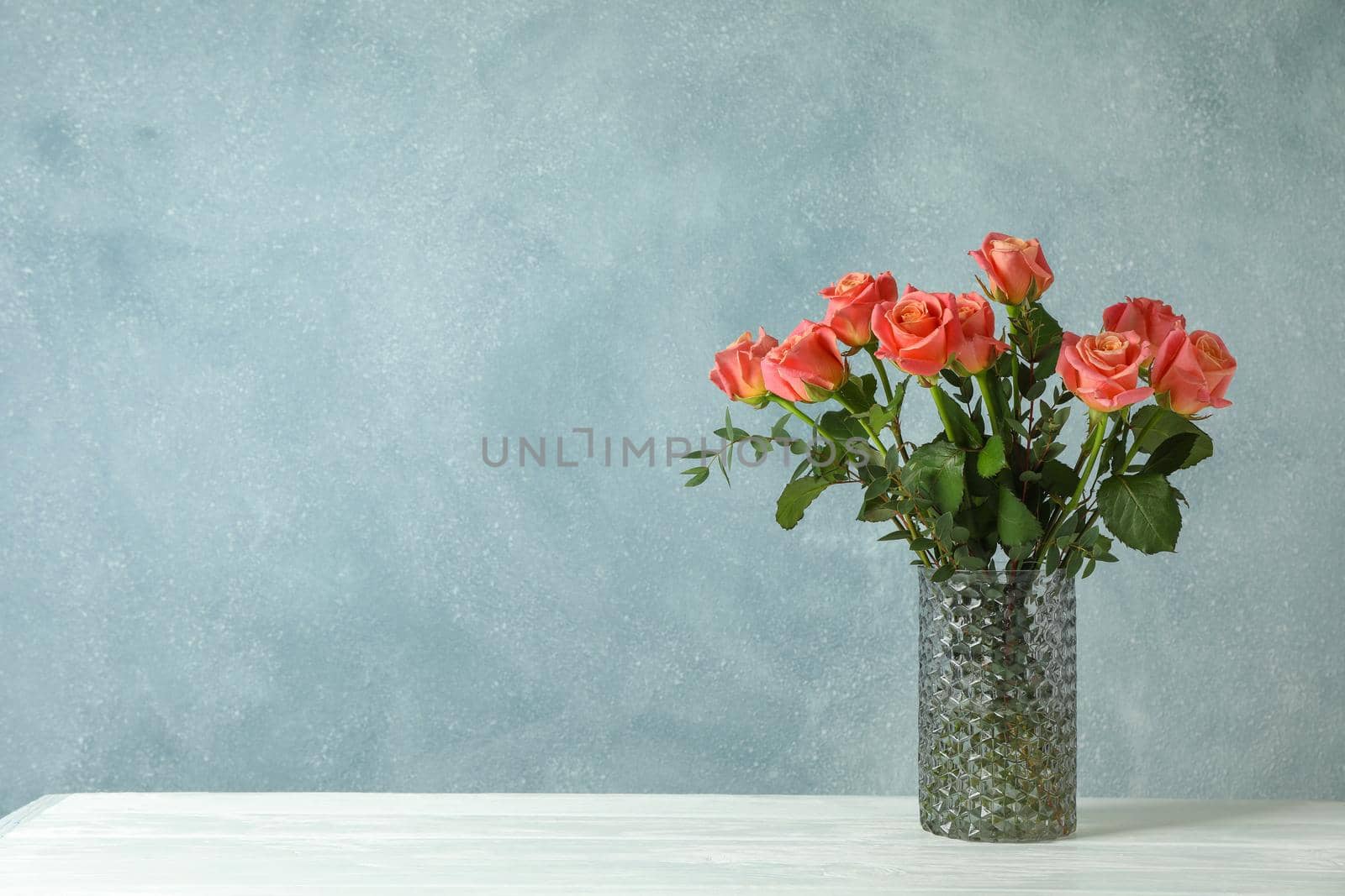 Vase with orange roses on white table against light background, space for text by AtlasCompany