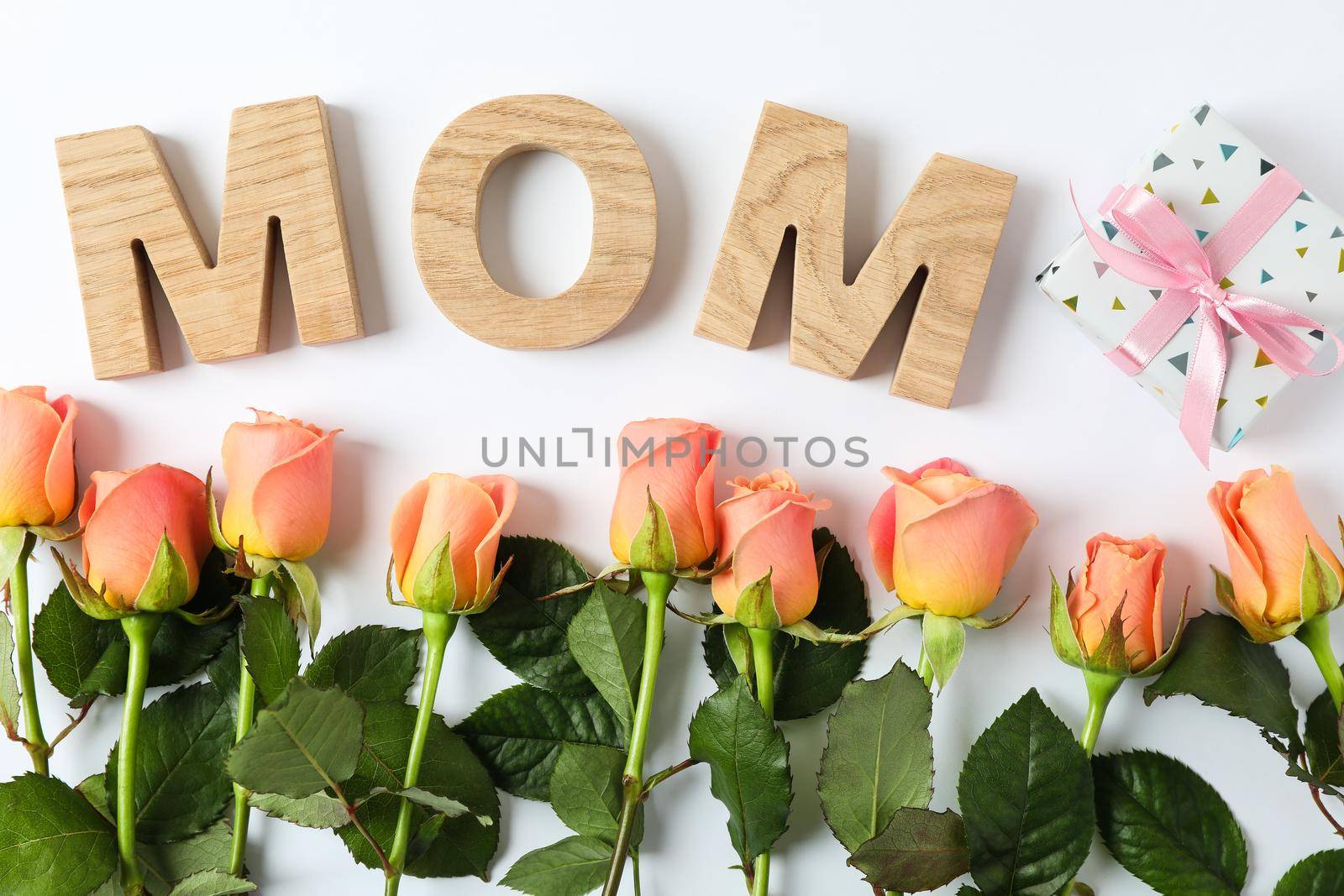 Inscription Mom with pink roses and gift on two tone background, top view