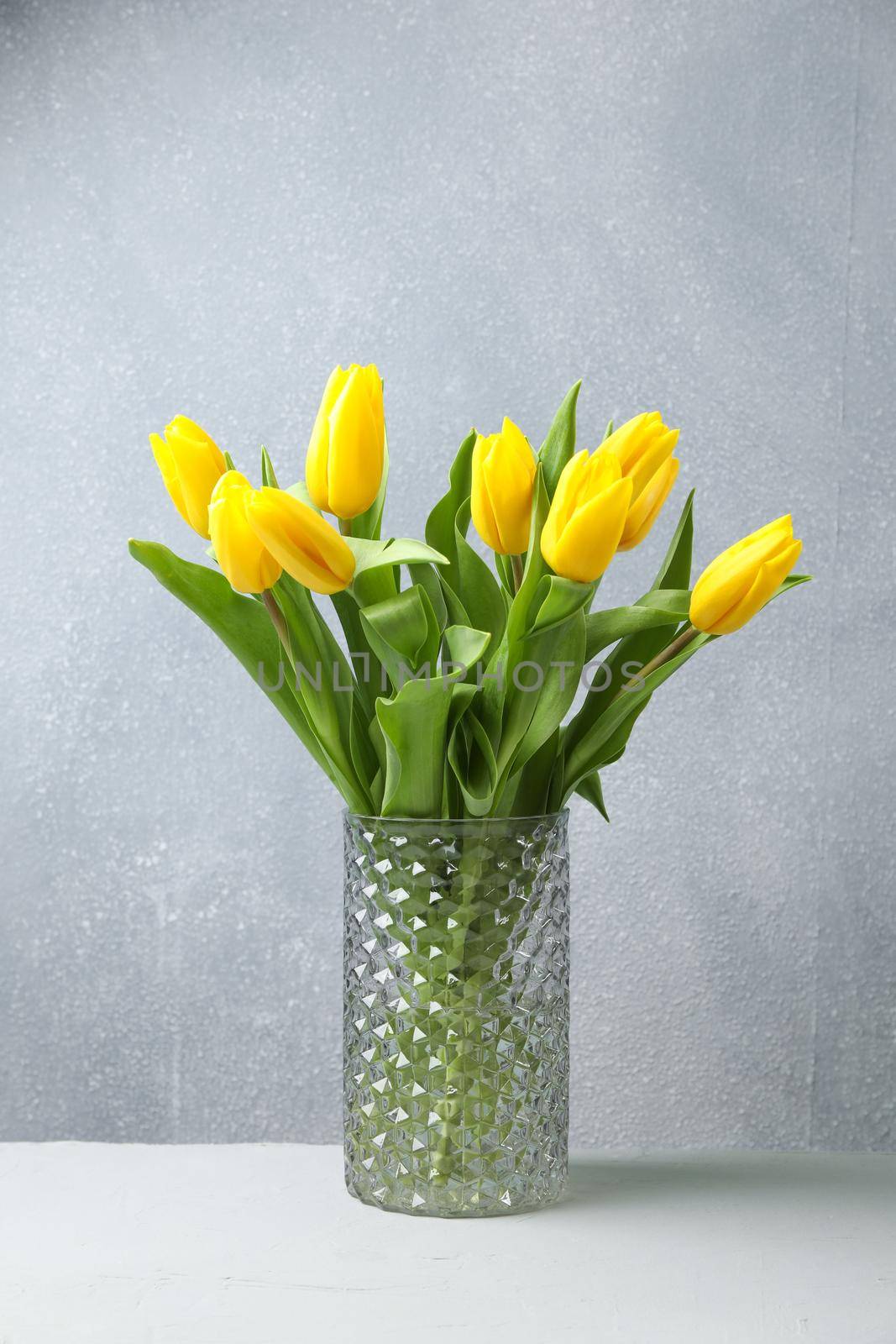 Beautiful yellow tulips in a glass vase on wooden table