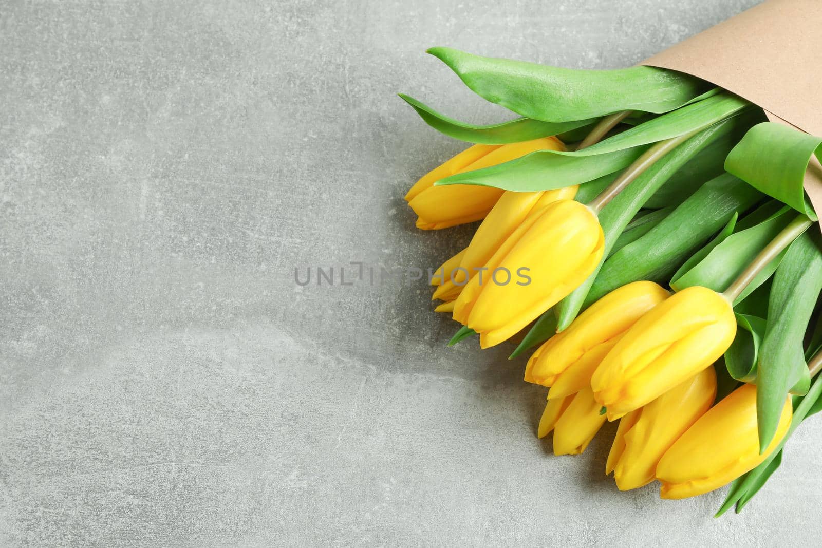 Beautiful bouquet of yellow tulips on grey background, top view. Space for text