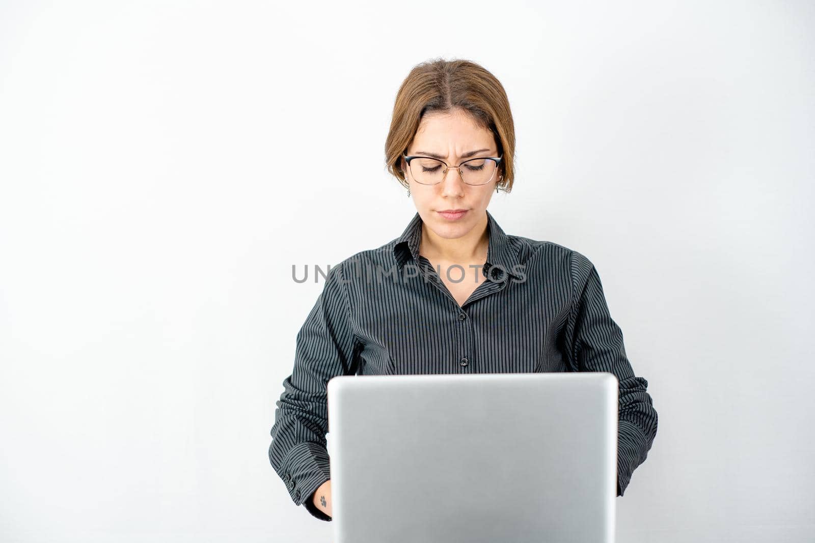 Business woman with dark shirt and glasses concentrated on computer work looks at the screen wearing work clothes isolated on copy space white background. Women in technological and communication jobs