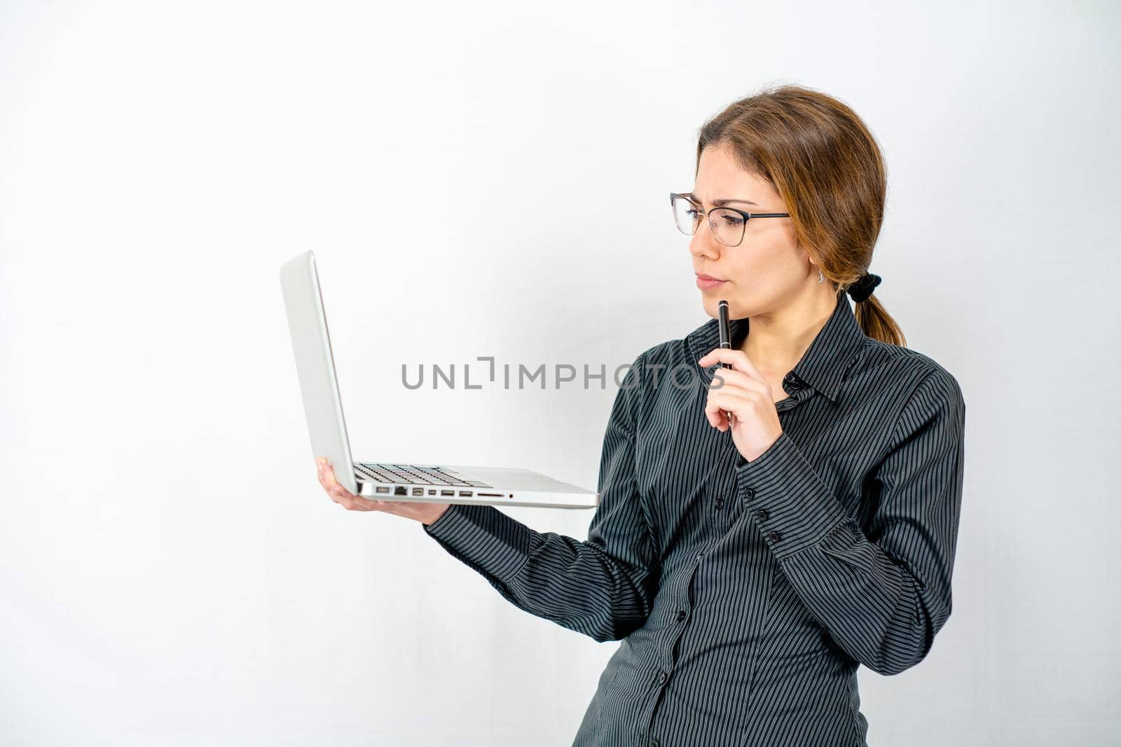 Business woman with dark shirt looking pensive at the laptop with eyeglasses and pen at the mouth. Concept of female sex leading to problem solving in the world of work and technologies