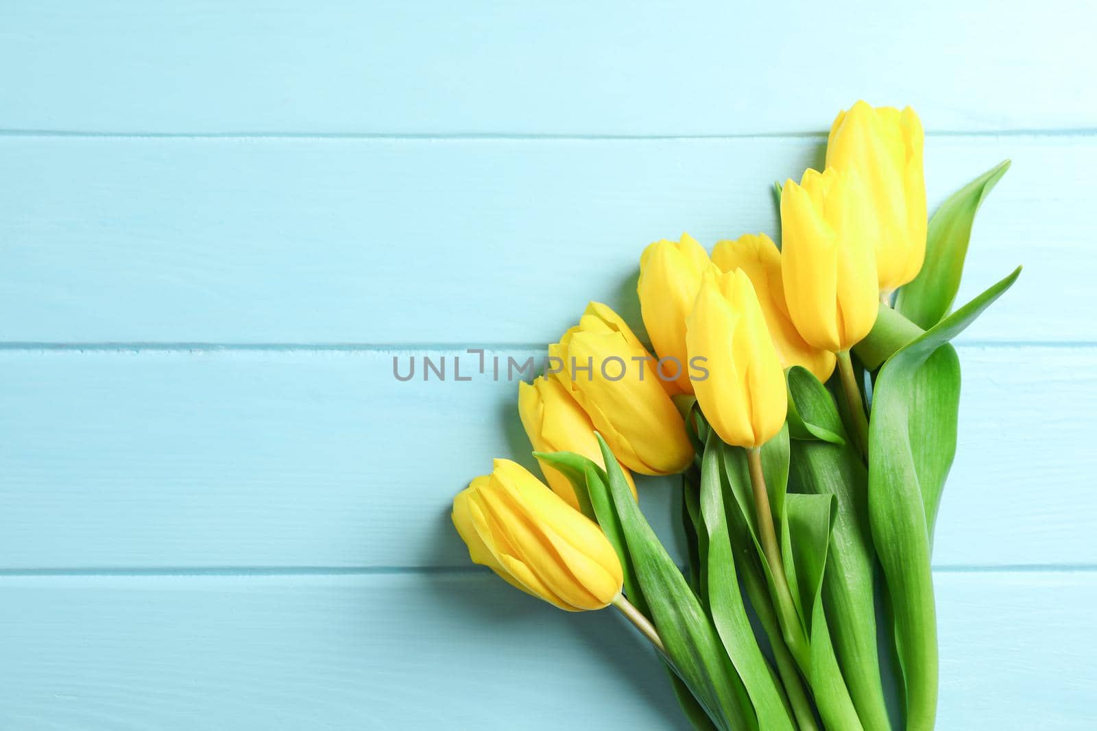 Beautiful bouquet of yellow tulips on wooden background, space for text