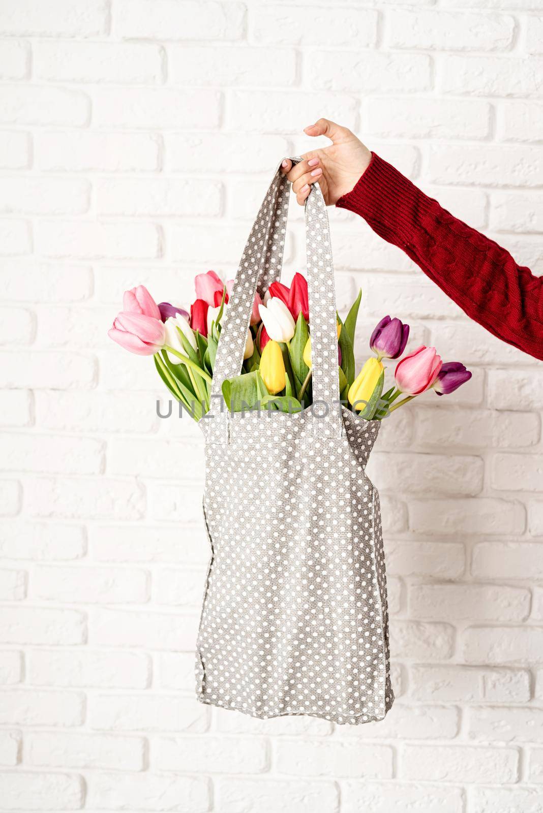 Eco friendly, zero waste concept. Spring shopping. Woman hand holding gray polka dot fabric bag with colorful tulips