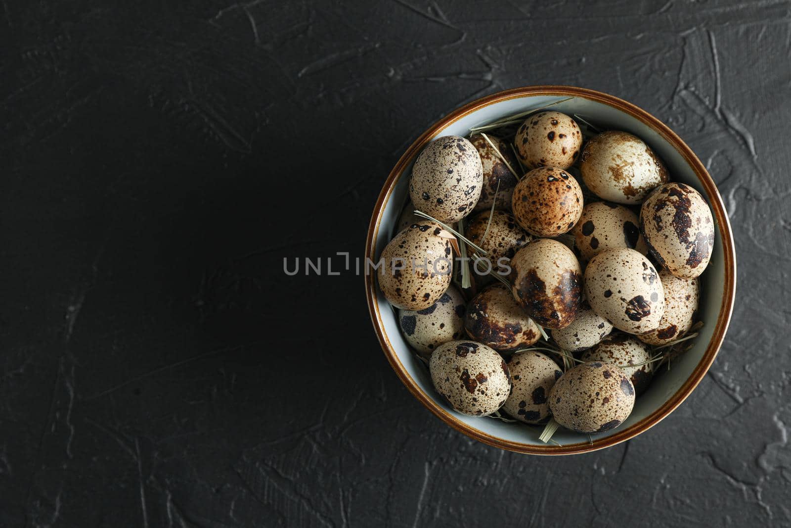 Many quail eggs in bowl on black background, space for text and top view