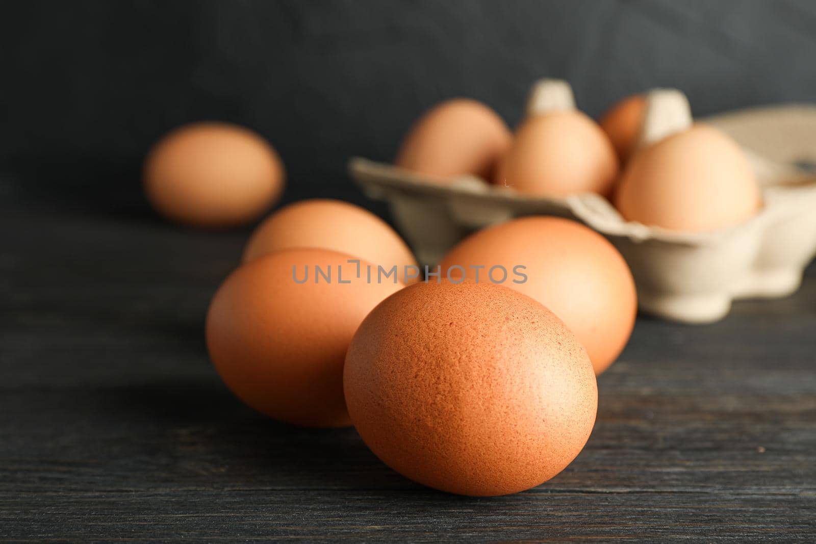 Brown chicken eggs in carton box on wooden table against black background, space for text and closeup