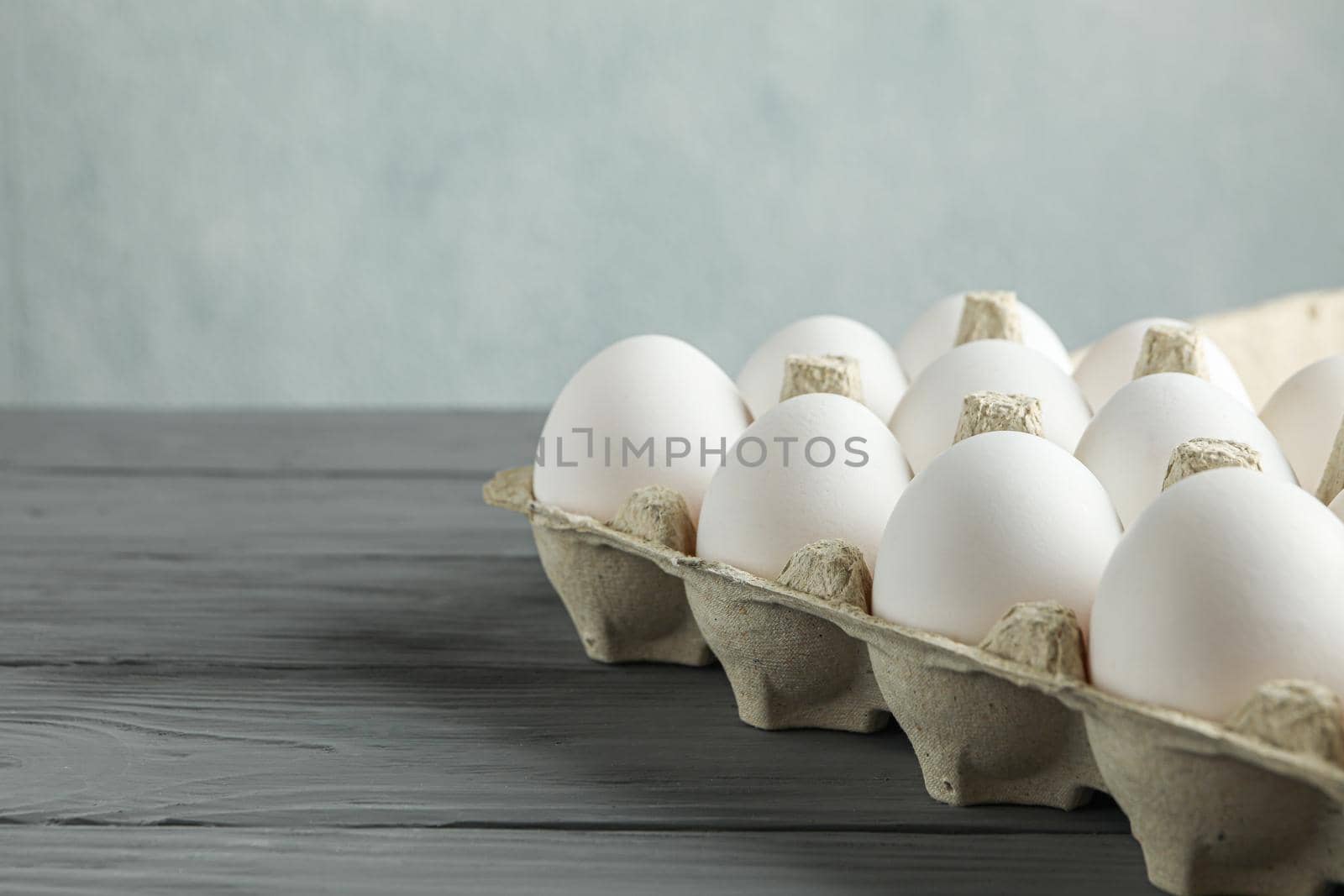 White chicken eggs in carton box on wooden table against light background, space for text