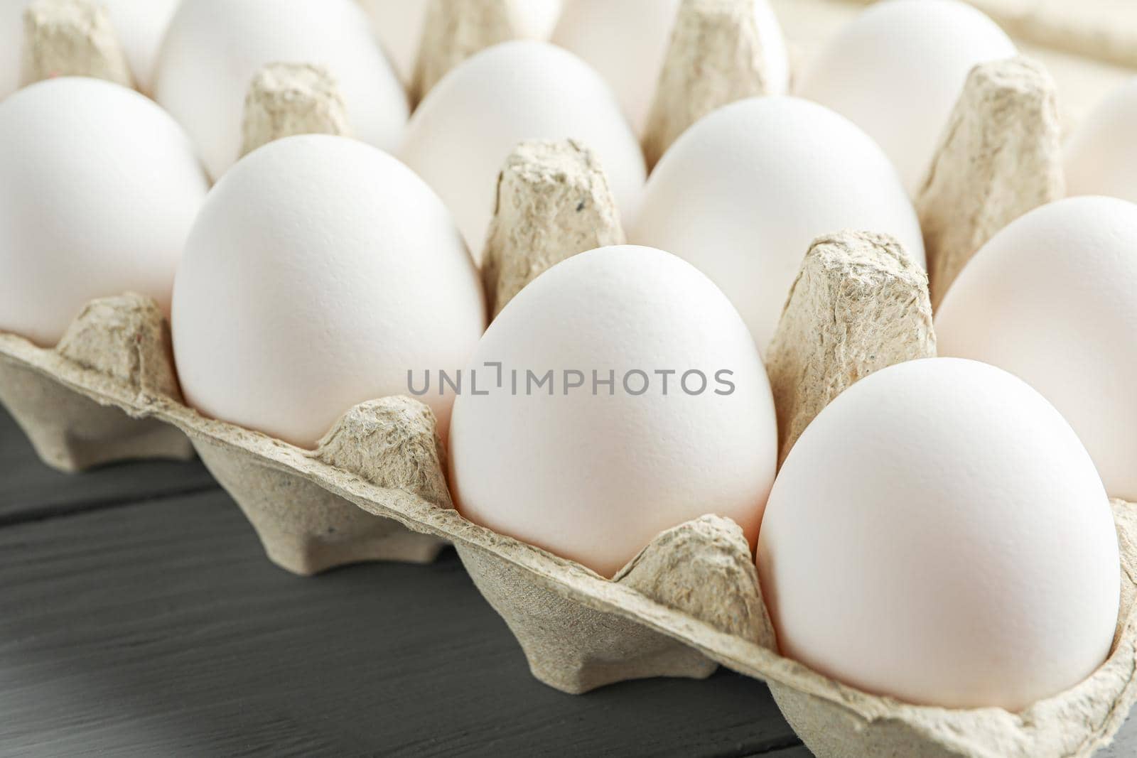 White chicken eggs in carton box on wooden table, space for text and closeup