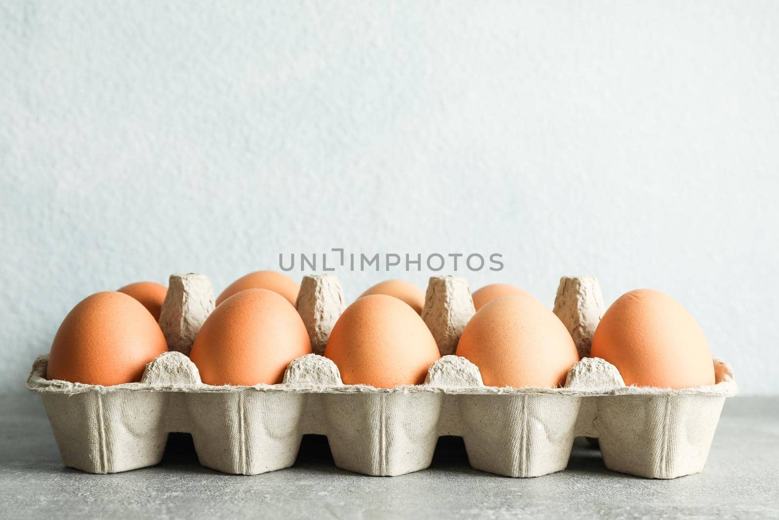 Chicken eggs in carton box on gray background, space for text