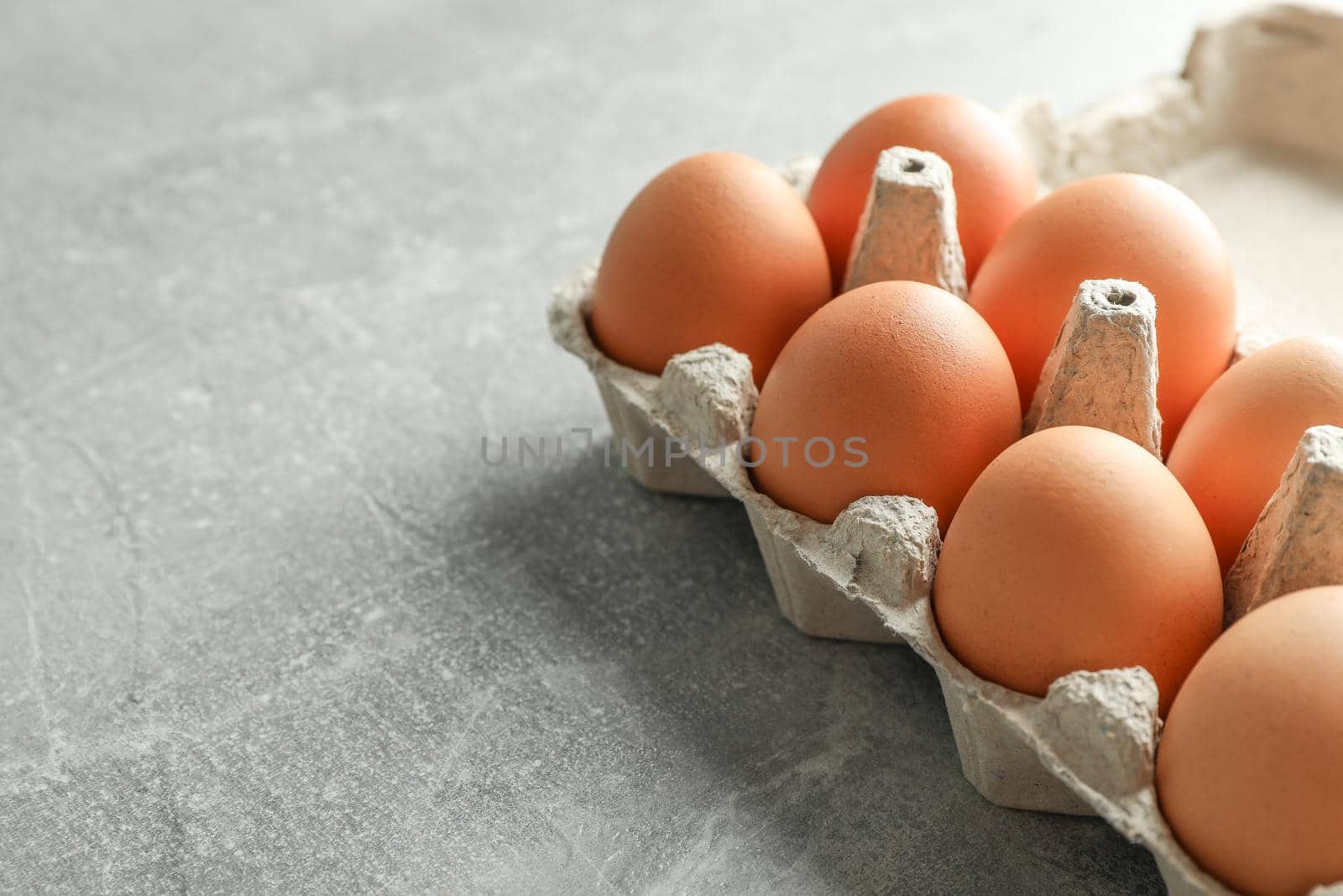 Chicken eggs in carton box on gray background, space for text