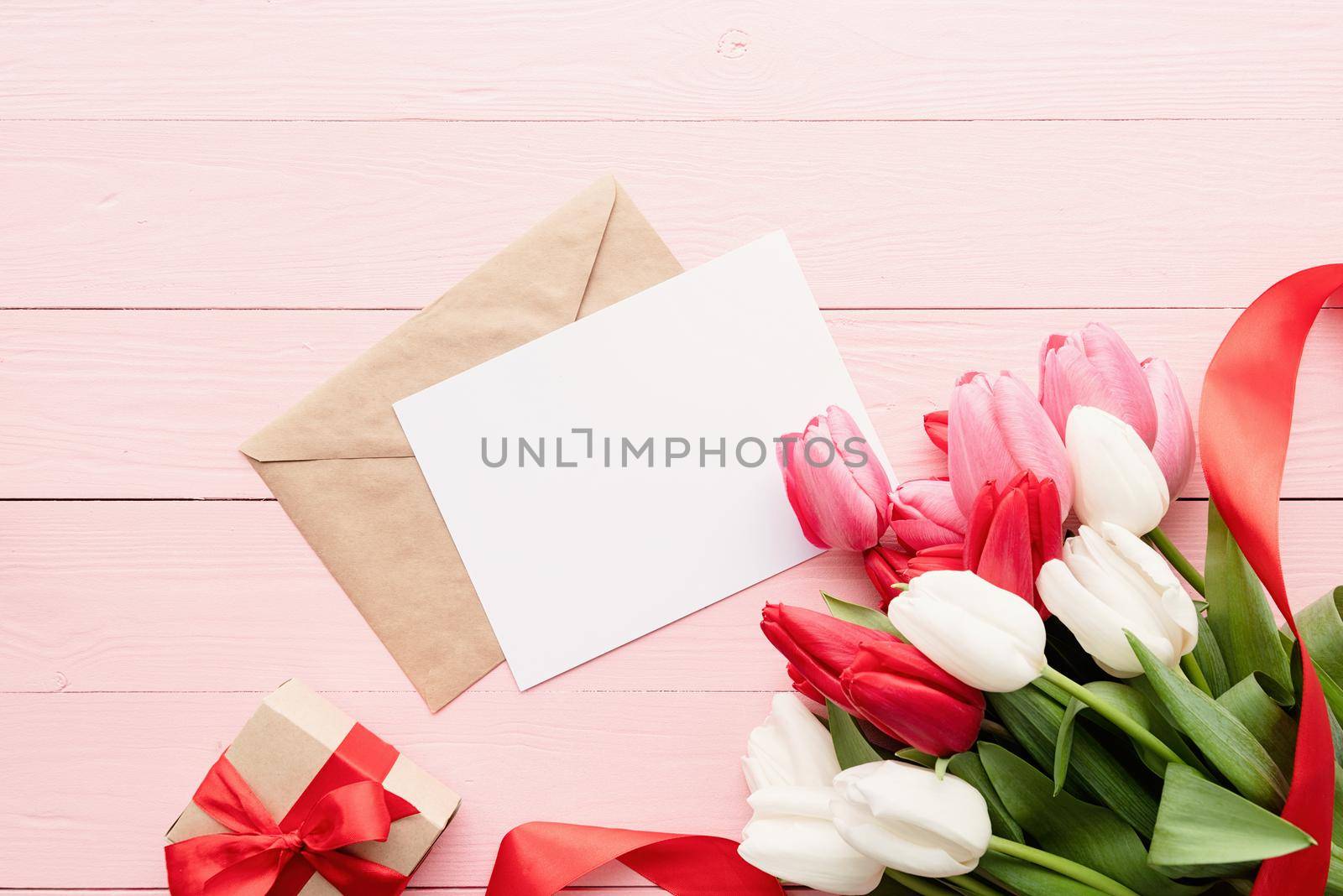 Frame mock up with Greeting card and envelope with colorful spring tulips top view over pink wooden background. Flat lay, top view.
