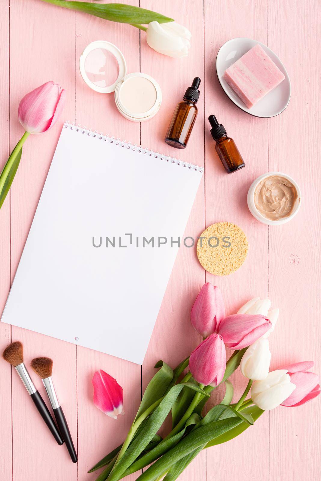 Spring and beauty. Top view of cosmetics and pink and white tulips with calendar or notepad for mock up flat lay on pink wooden background