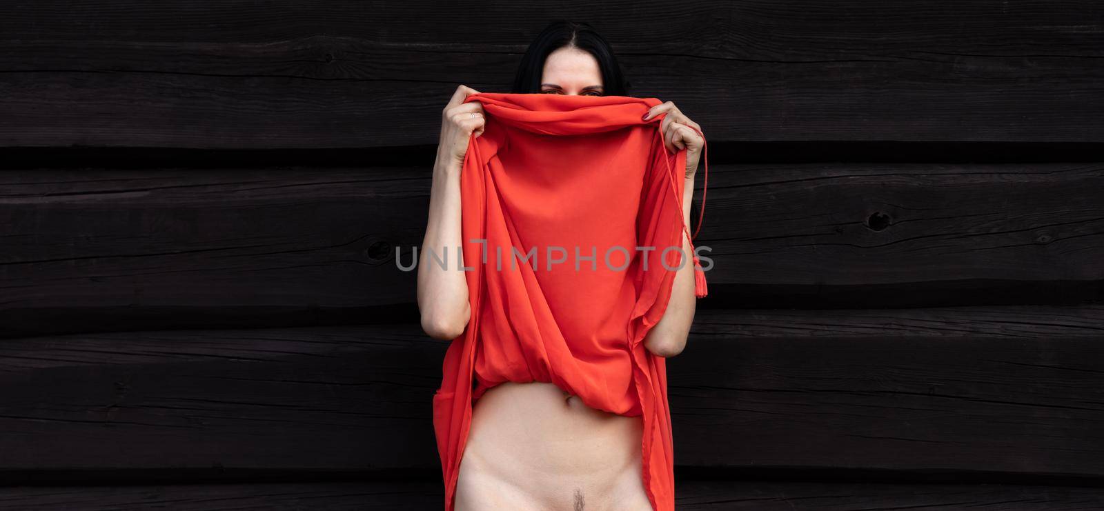 Young woman in red dressand naked body on the background of a wooden house wall