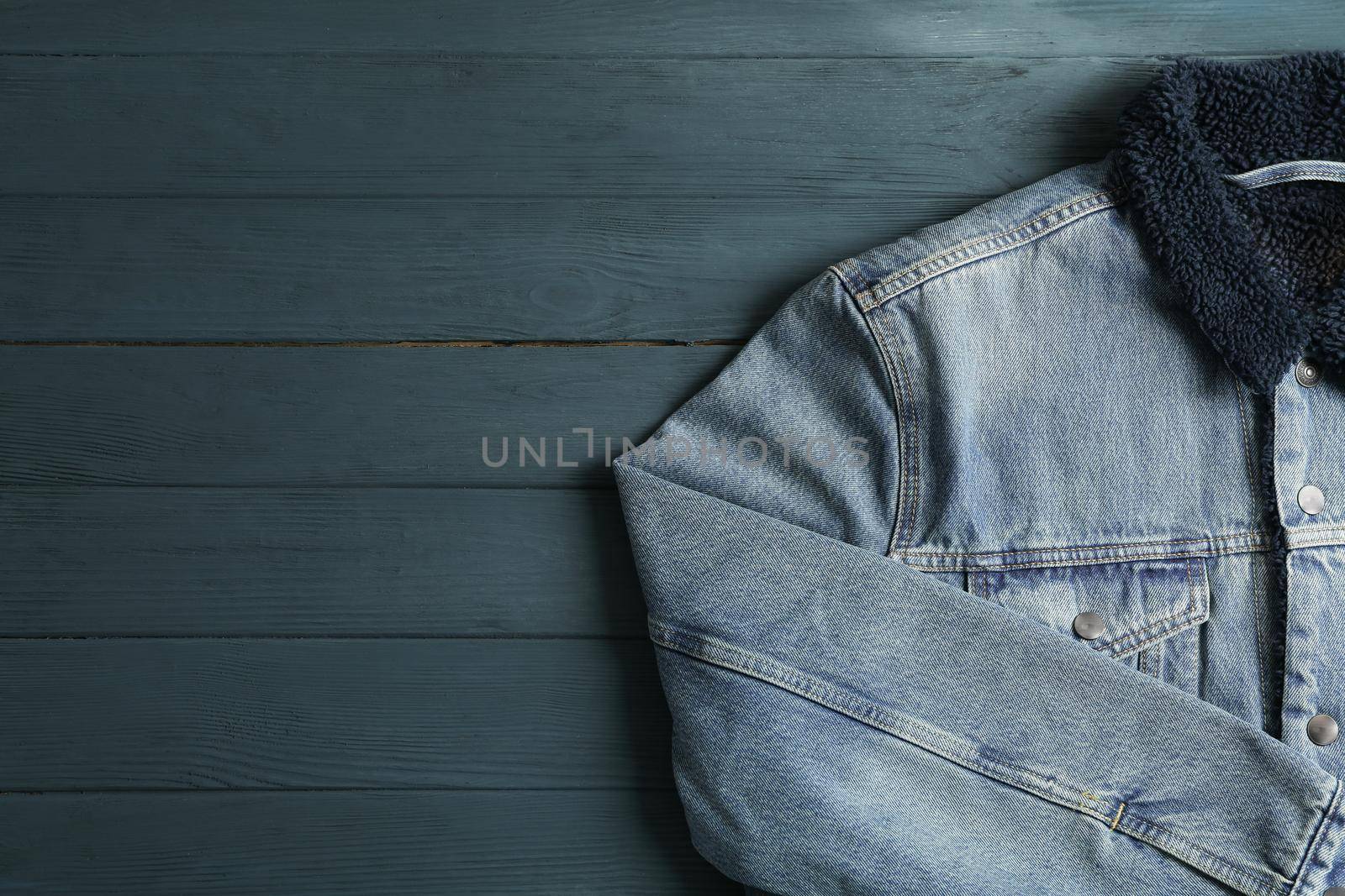 Denim jacket on wooden background, space for text