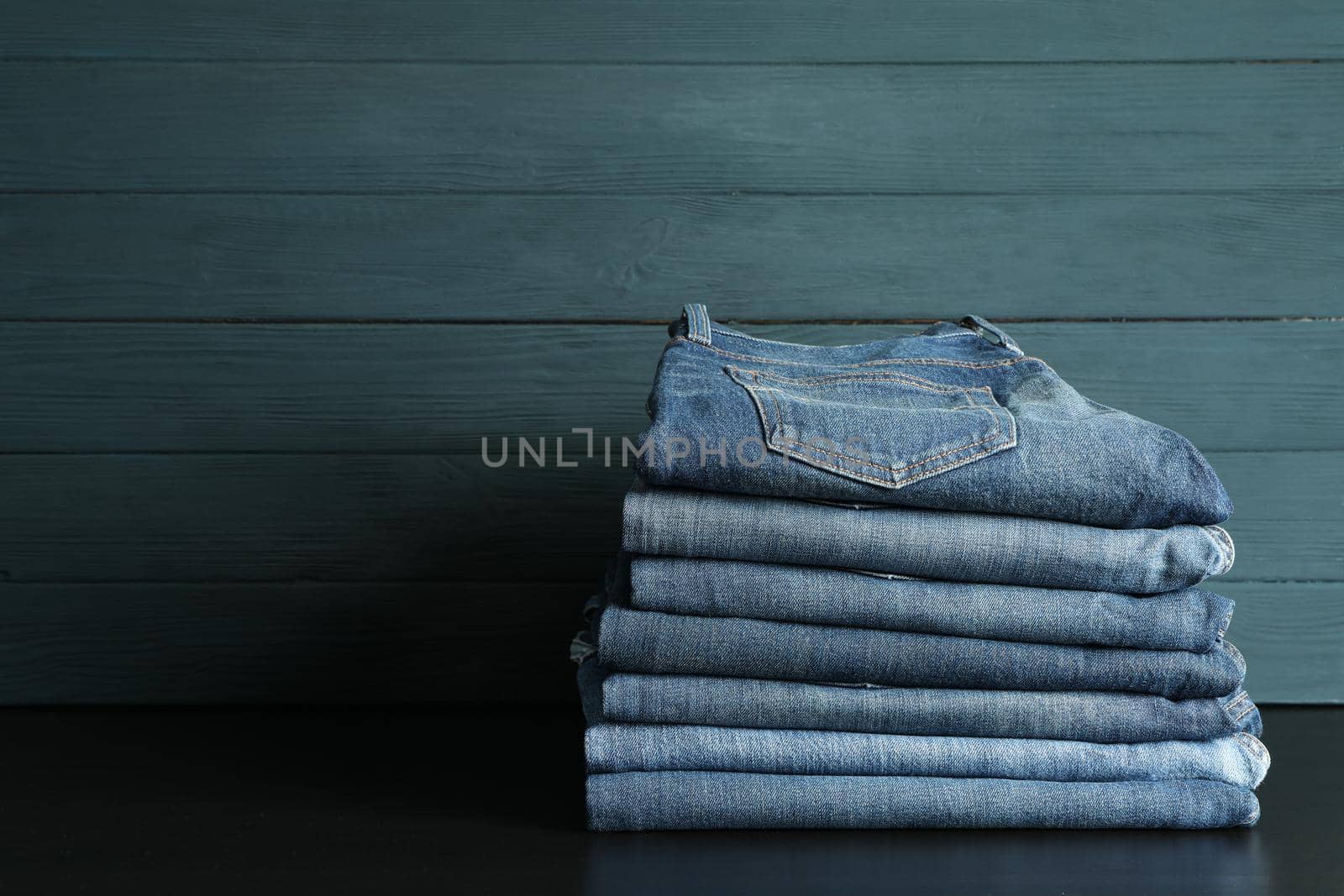 Stack of jeans pants on black table, space for text