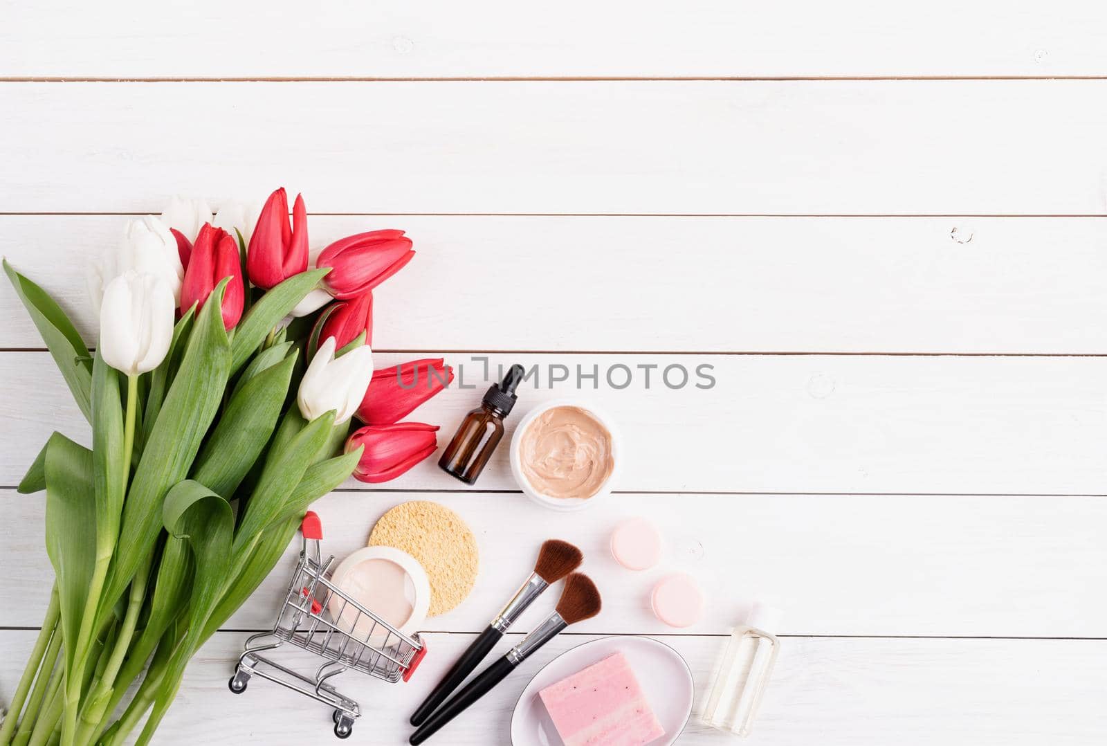 Top view of cosmetics with pink tulips flat lay on white wooden background by Desperada