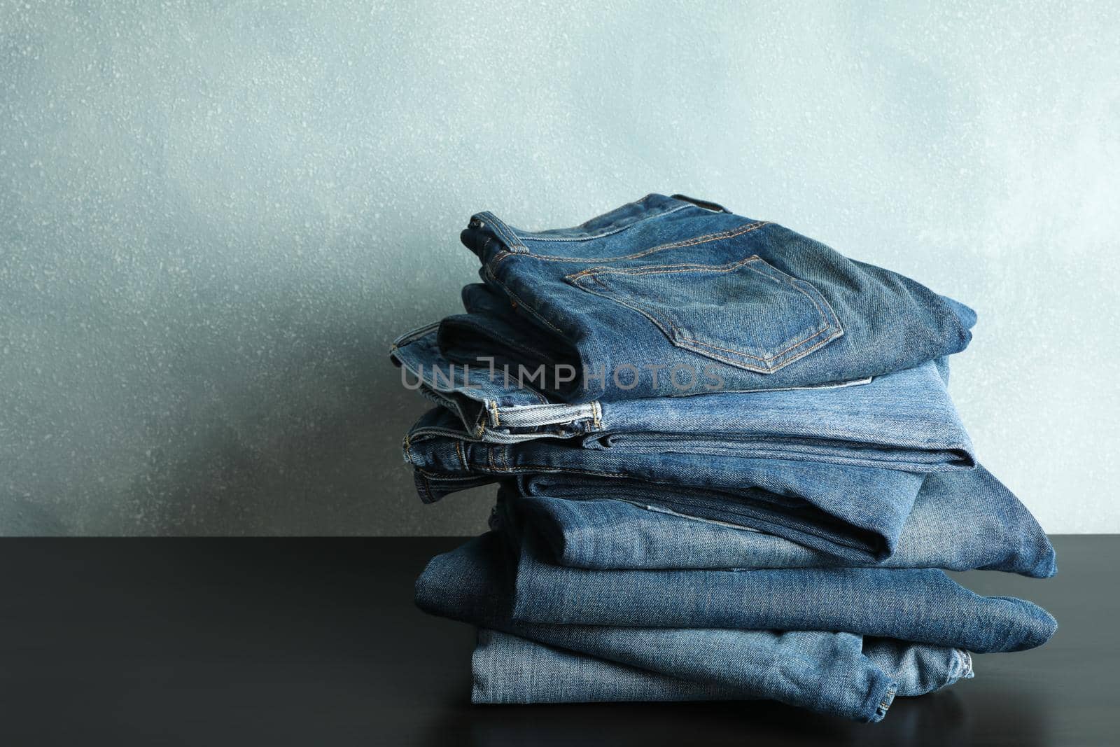 Stack of jeans pants on black table, space for text