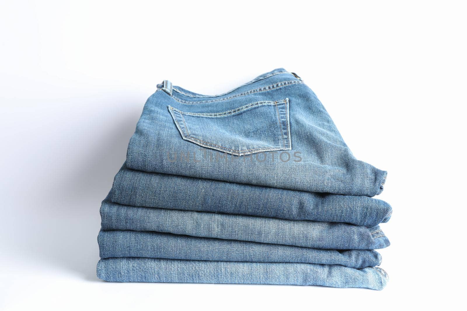 Stack of jeans pants on white background, space for text