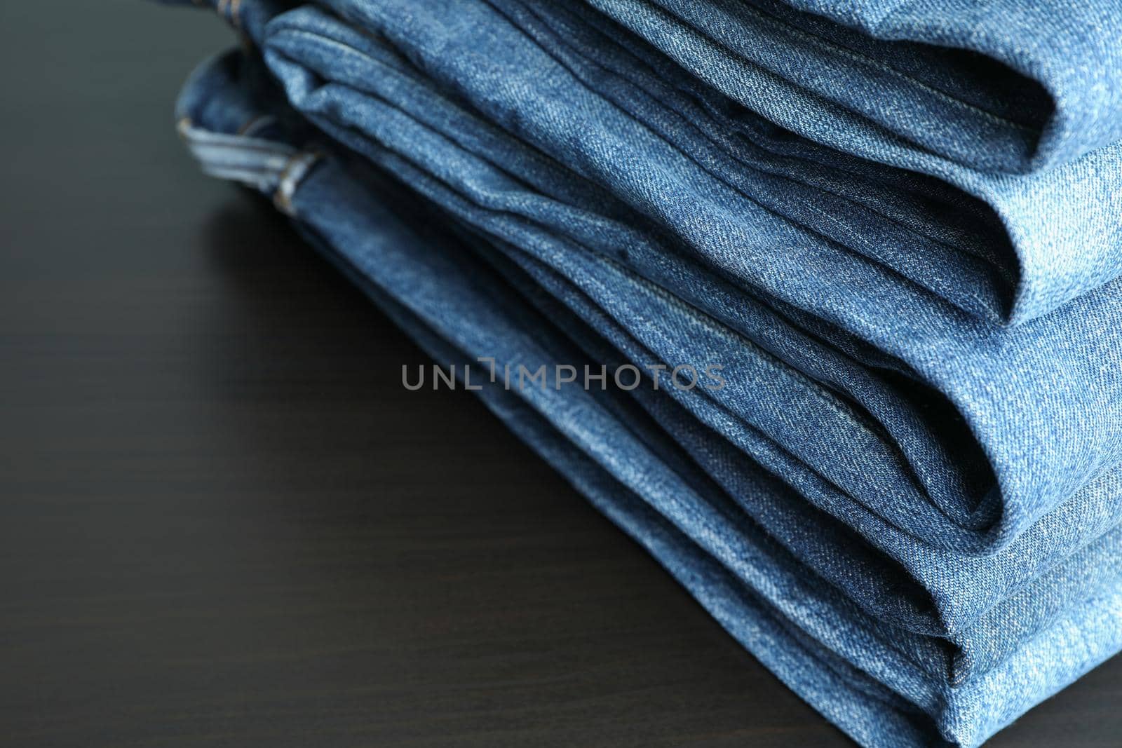 Stack of jeans pants on black table, space for text