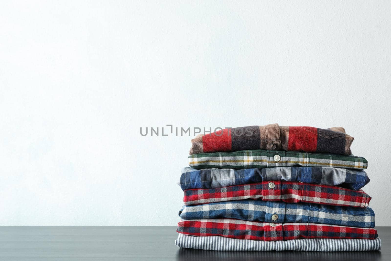 Stack of different shirts on black table, space for text