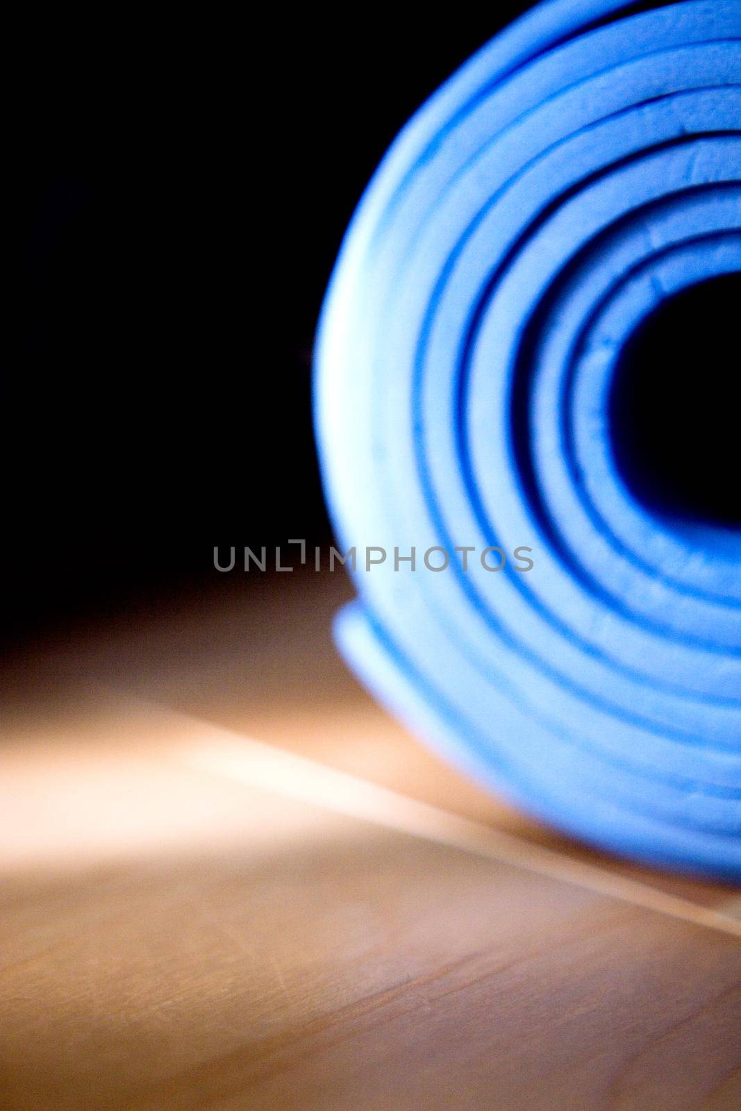 Yoga and Pilates mat rolled up on the floor by GemaIbarra