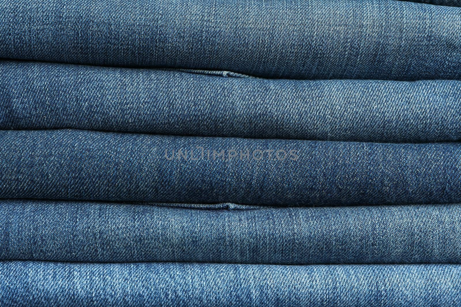 Stack of jeans pants textured background, close up by AtlasCompany