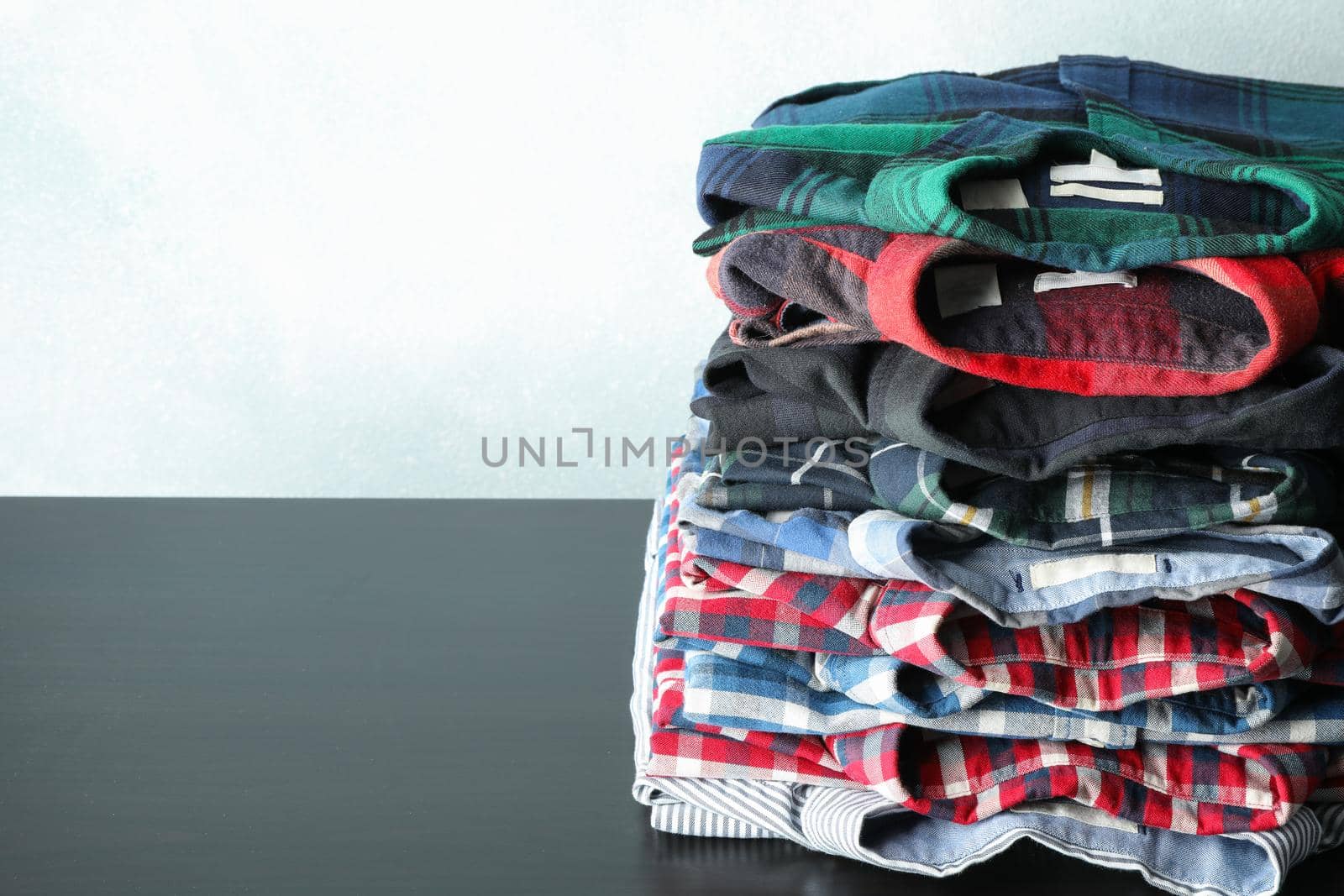 Stack of different shirts on black table, space for text