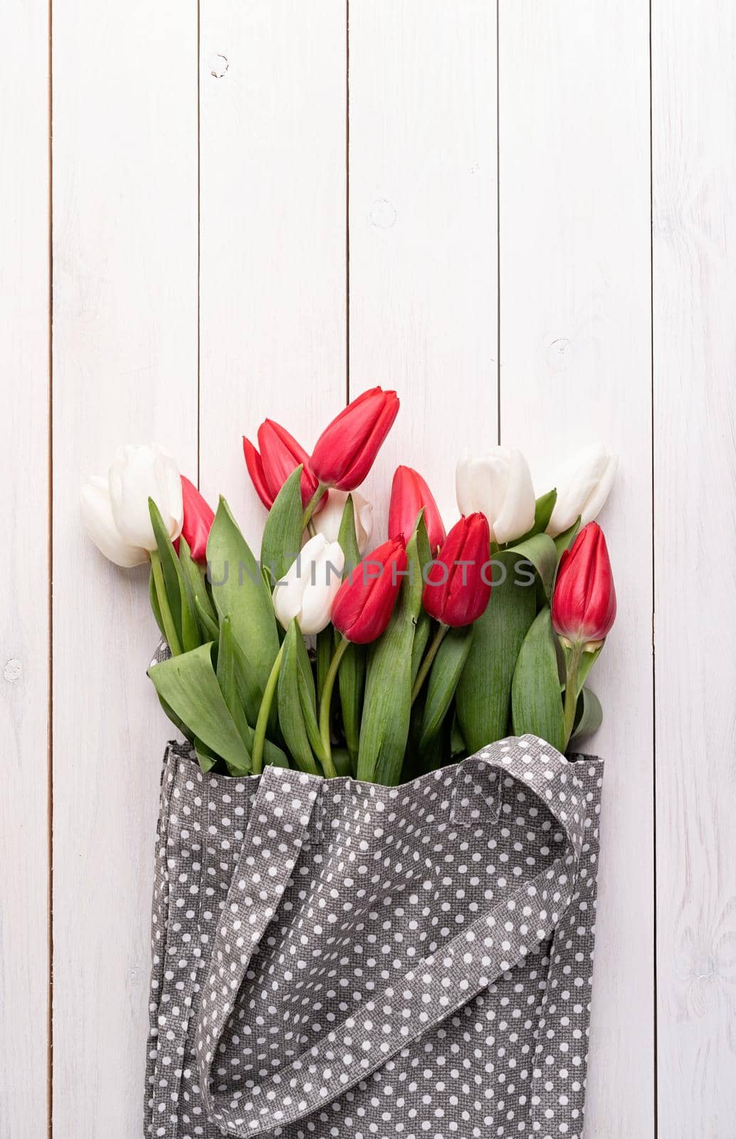 Eco friendly, zero waste concept. Gray fabric bag ful of colorful tulips on white wooden background