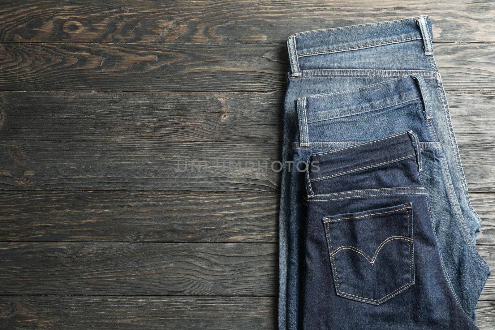 Different jeans folded on a wooden background, space for text by AtlasCompany
