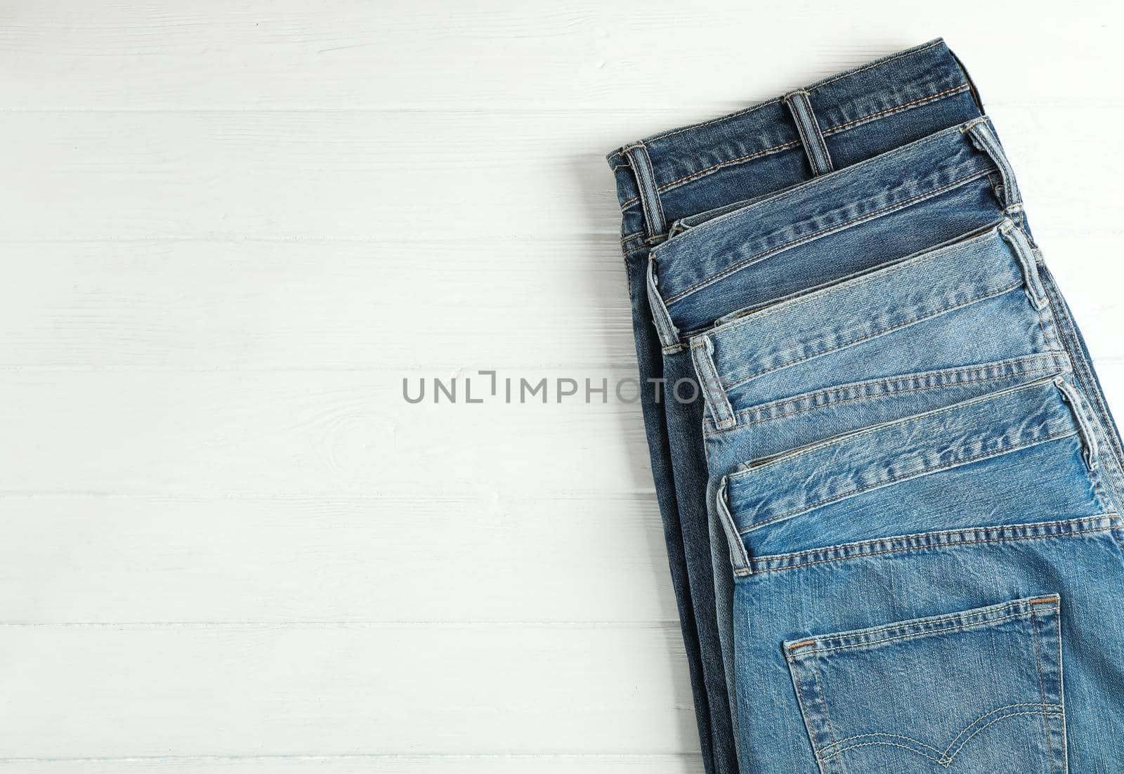 Different jeans folded on a white wooden background, space for text by AtlasCompany