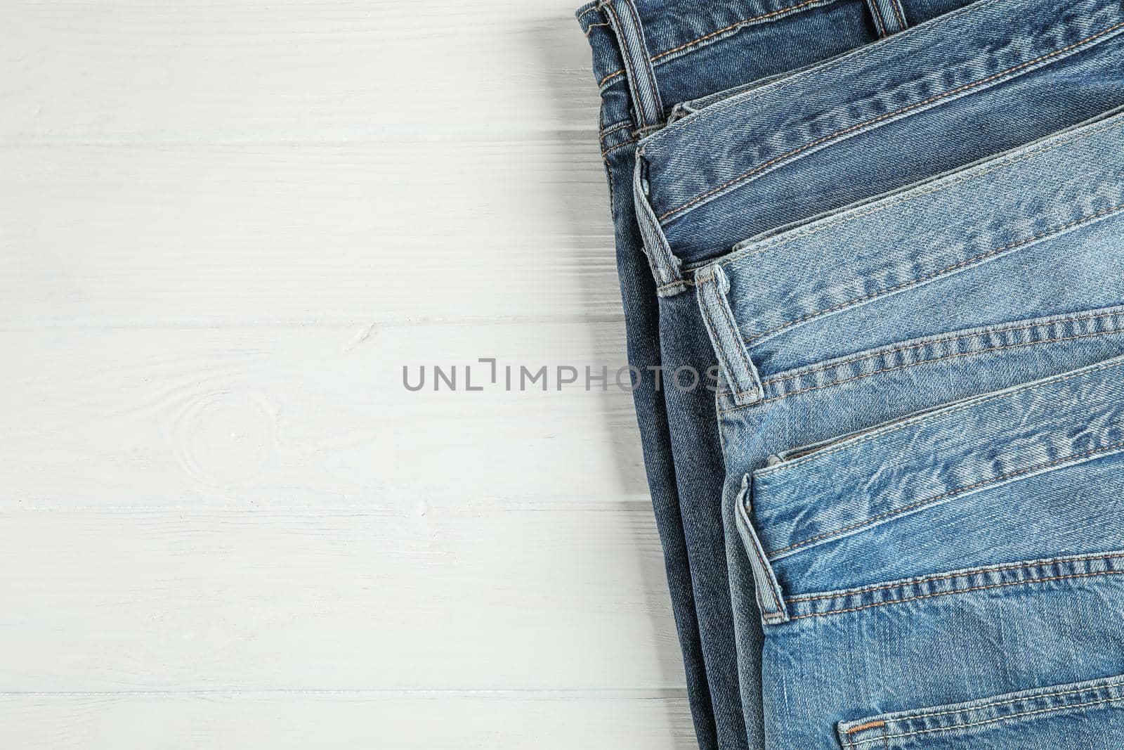 Different jeans folded on a white wooden background, space for text by AtlasCompany