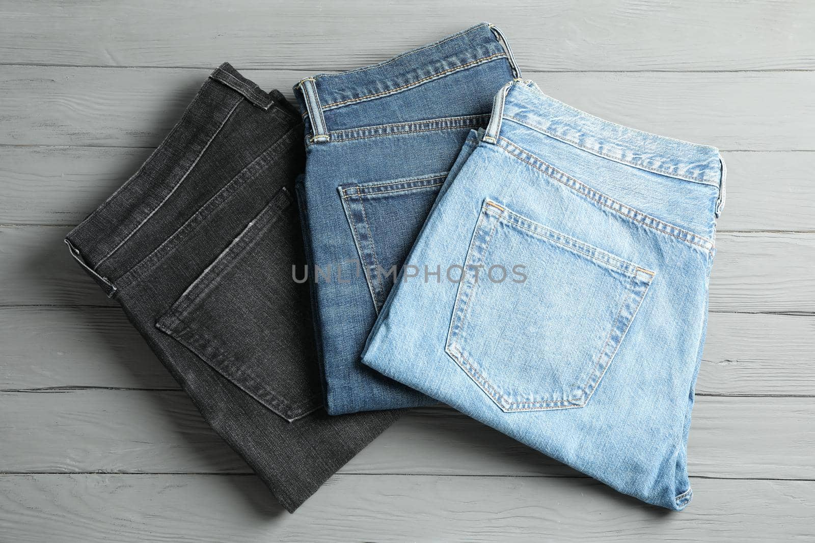 Different jeans on grey wooden background, space for text