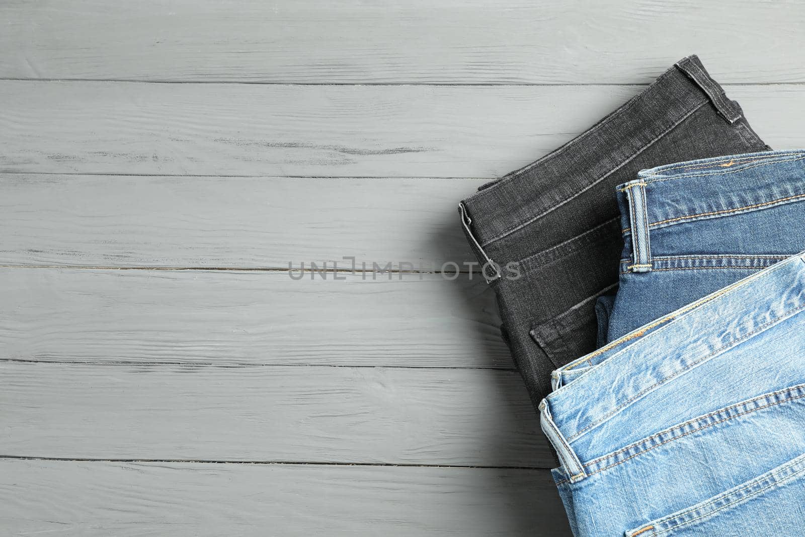 Different jeans on grey wooden background, space for text by AtlasCompany