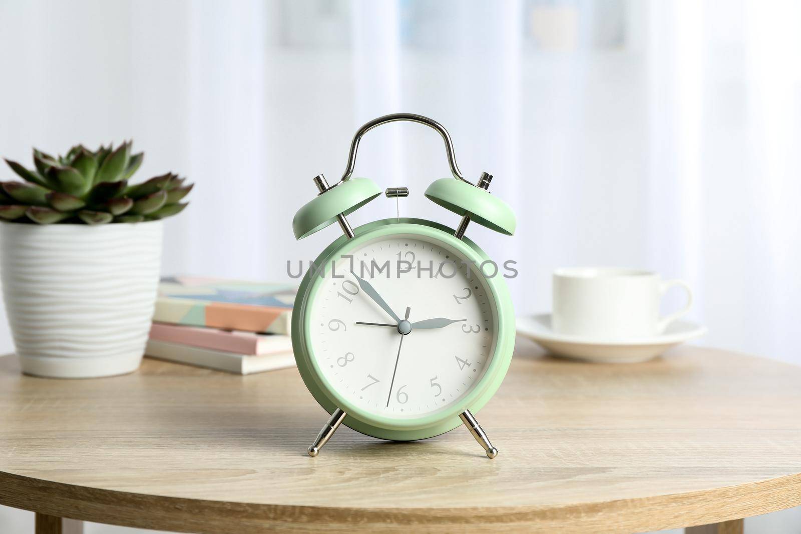 Beautiful retro alarm clock with cup of coffee, succulent plant and books on table against light background by AtlasCompany