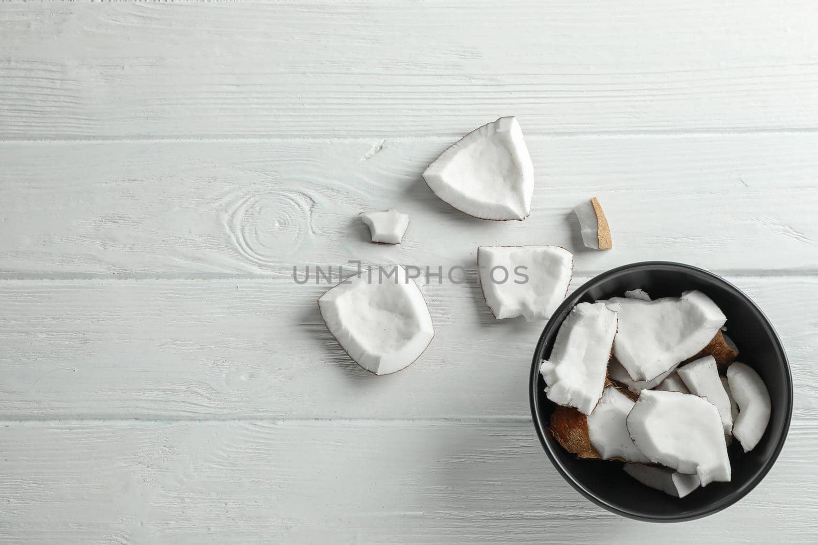 Plate with coconut pieces on white wooden background, space for text
