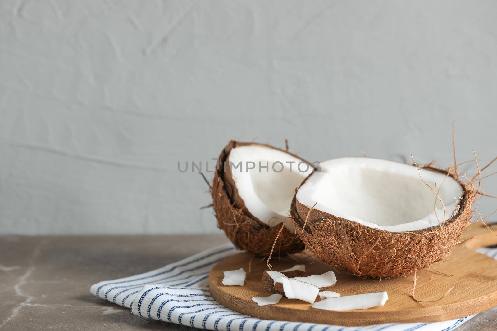 Cutting board with split coconut on table against grey background