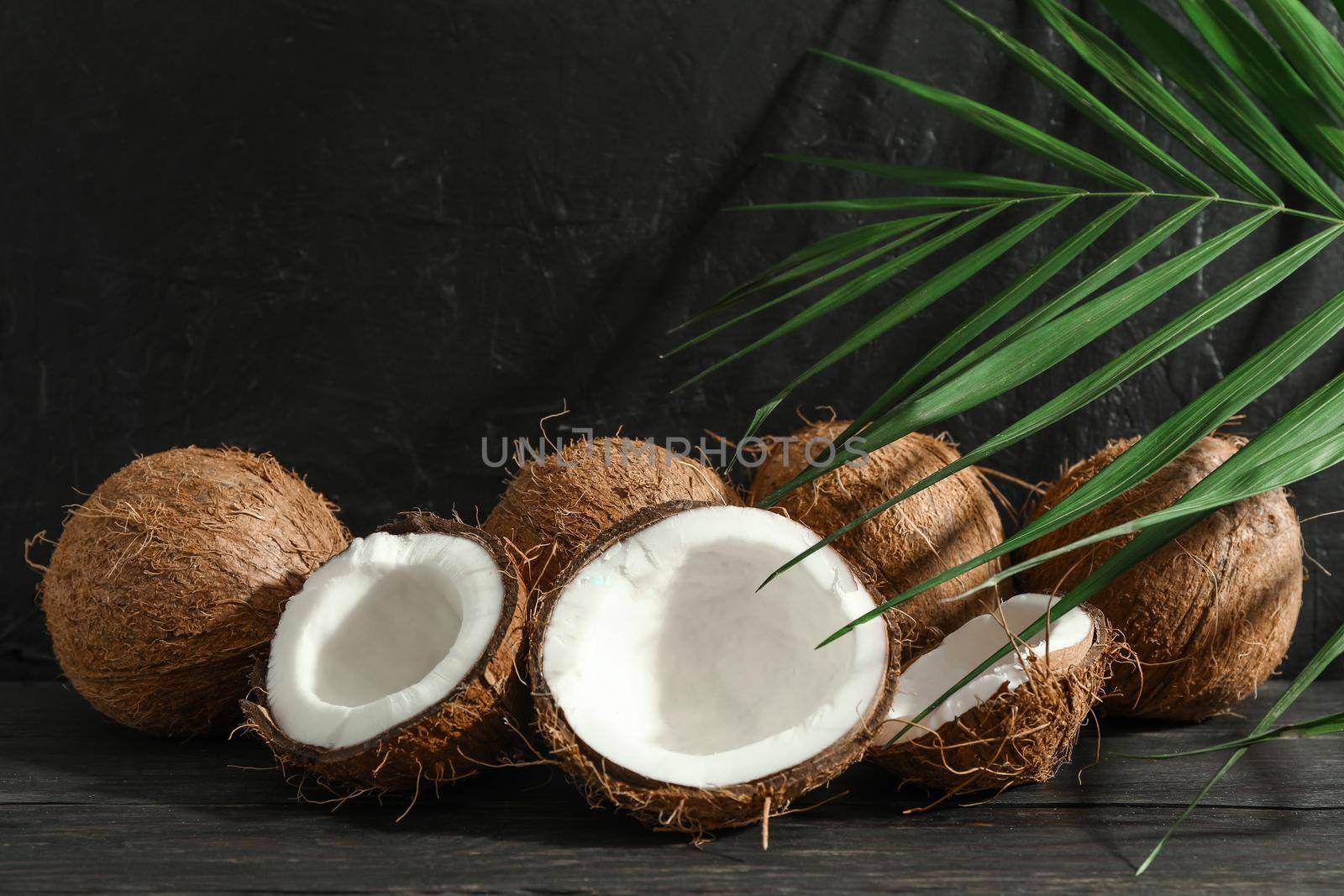 Coconuts with palm branch on wooden table against black background