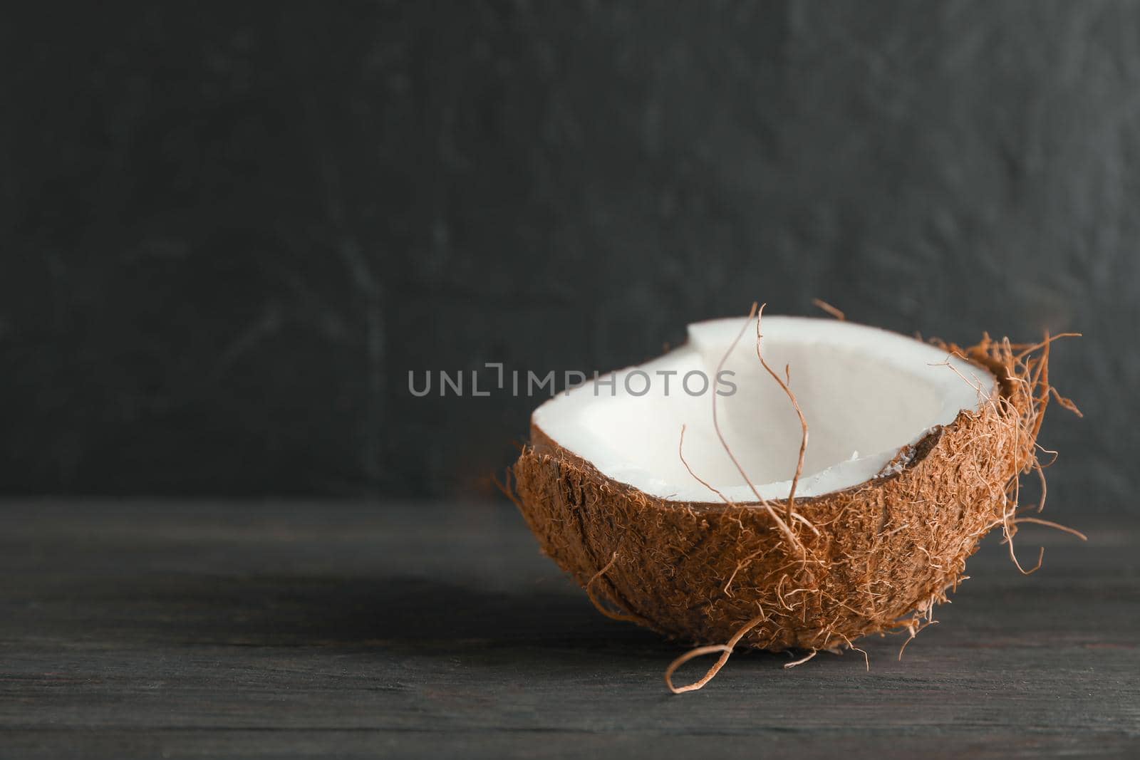 Half tropical coconut on wooden table against black background, space for text