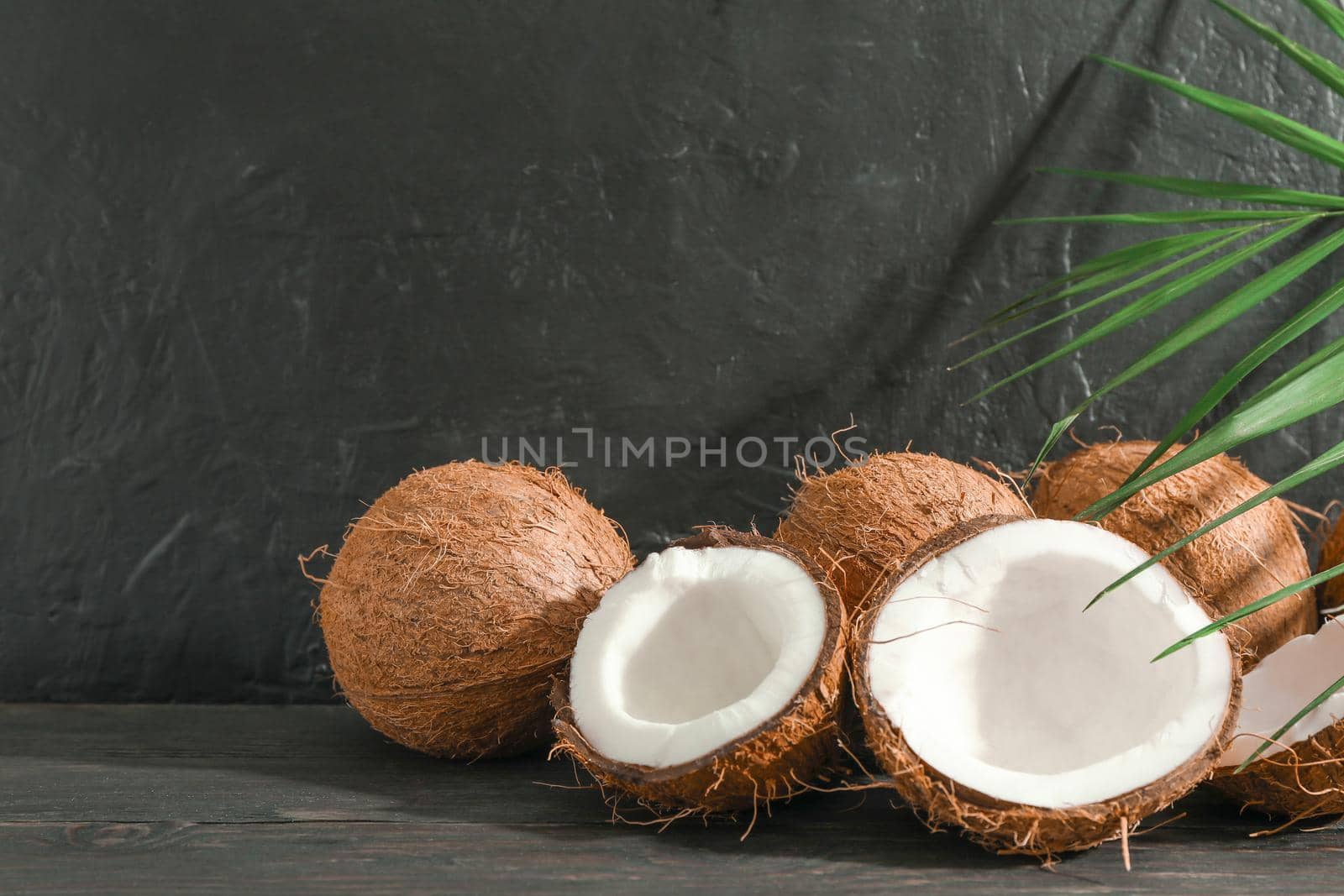 Coconuts with palm branch on wooden table against black background by AtlasCompany