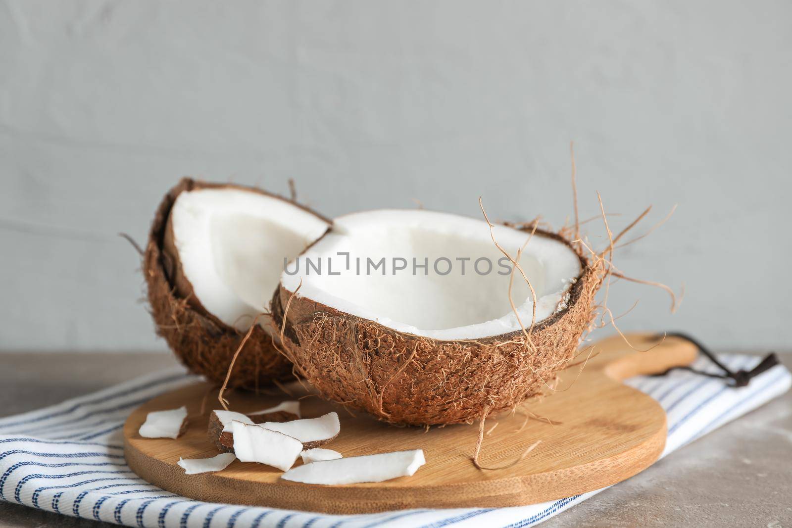 Cutting board with split coconut on table against grey background