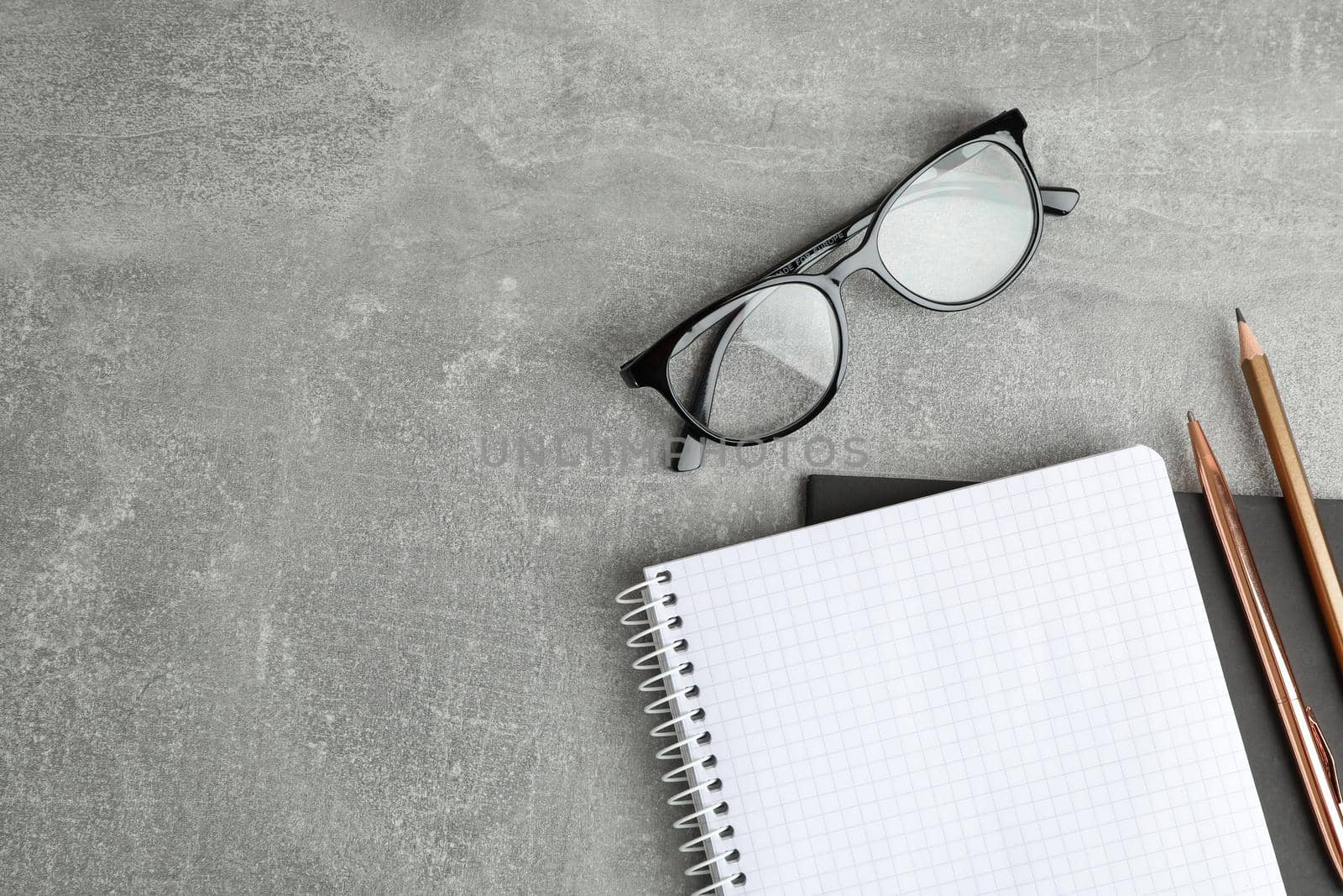 Copybooks, glasses and pencil on grey table, space for text