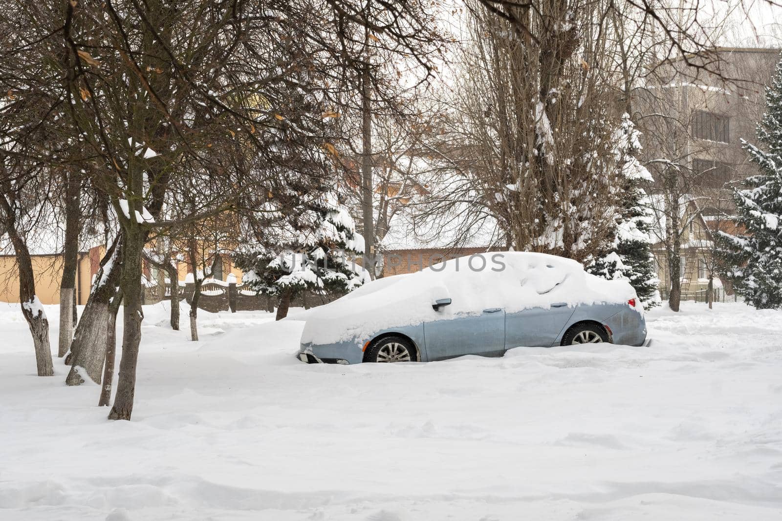 Stuck cars under the snow and ice. City street after blizzard. Buried vehicle in snowdrift on the road. Parking lots in winter after heavy snowfall. Uncleaned roads. Record-breaking amounts of snow.