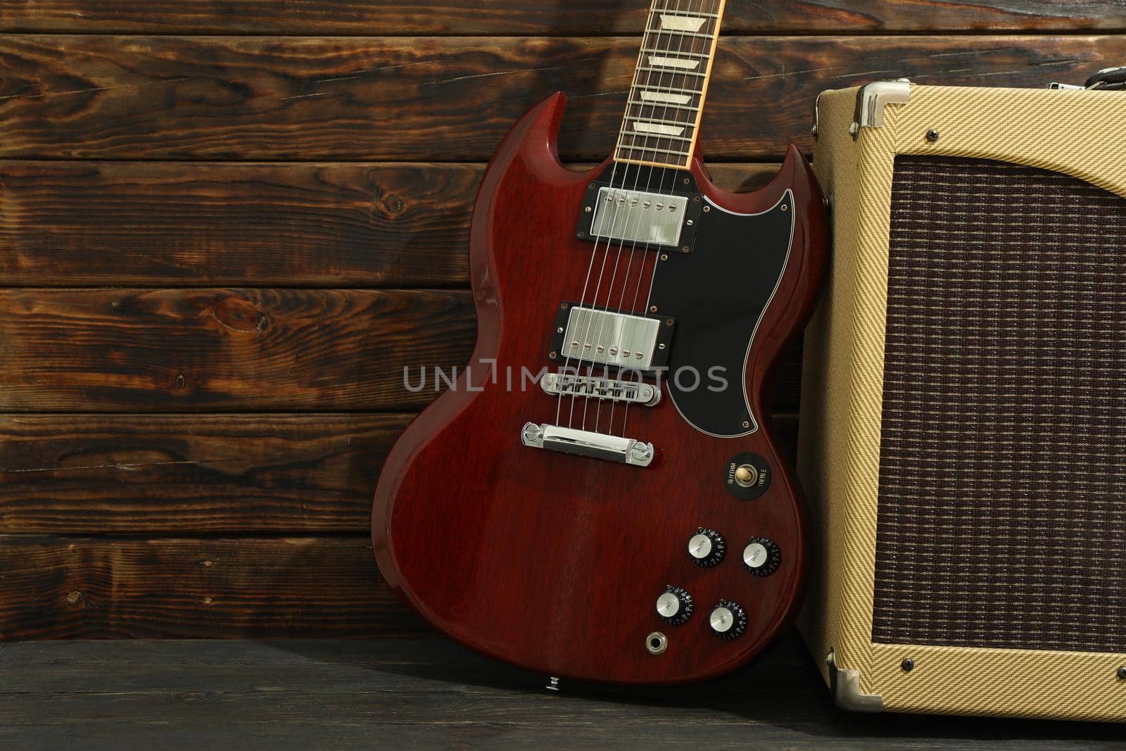 Beautiful six - string electric guitar with amplifier against wooden background, space for text