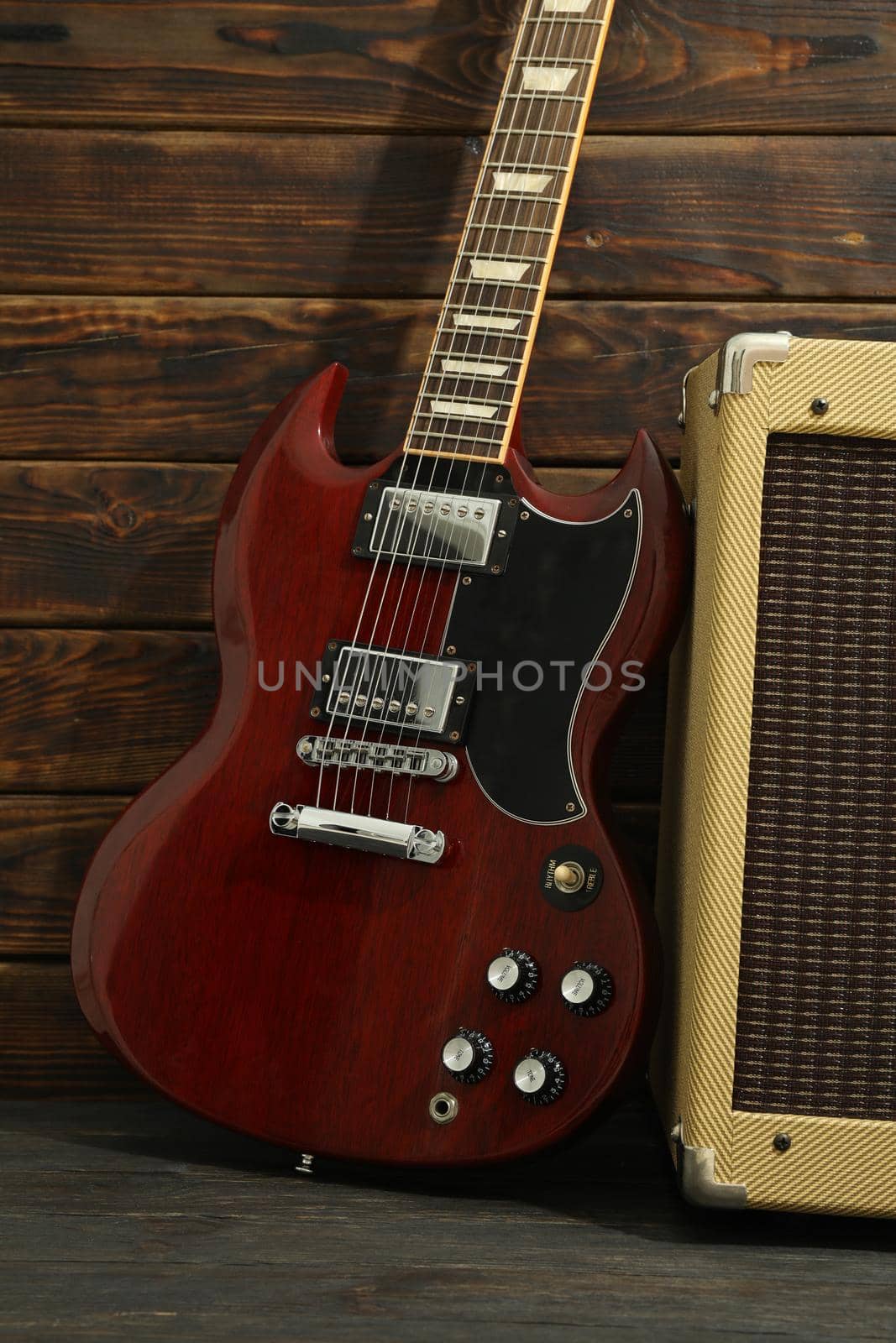Beautiful six - string electric guitar with amplifier against wooden background by AtlasCompany