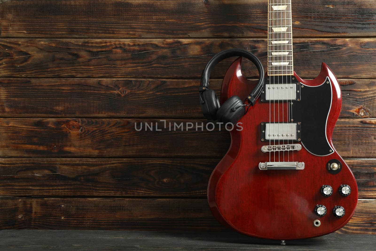 Beautiful six - string electric guitar with headphones against wooden background, space for text