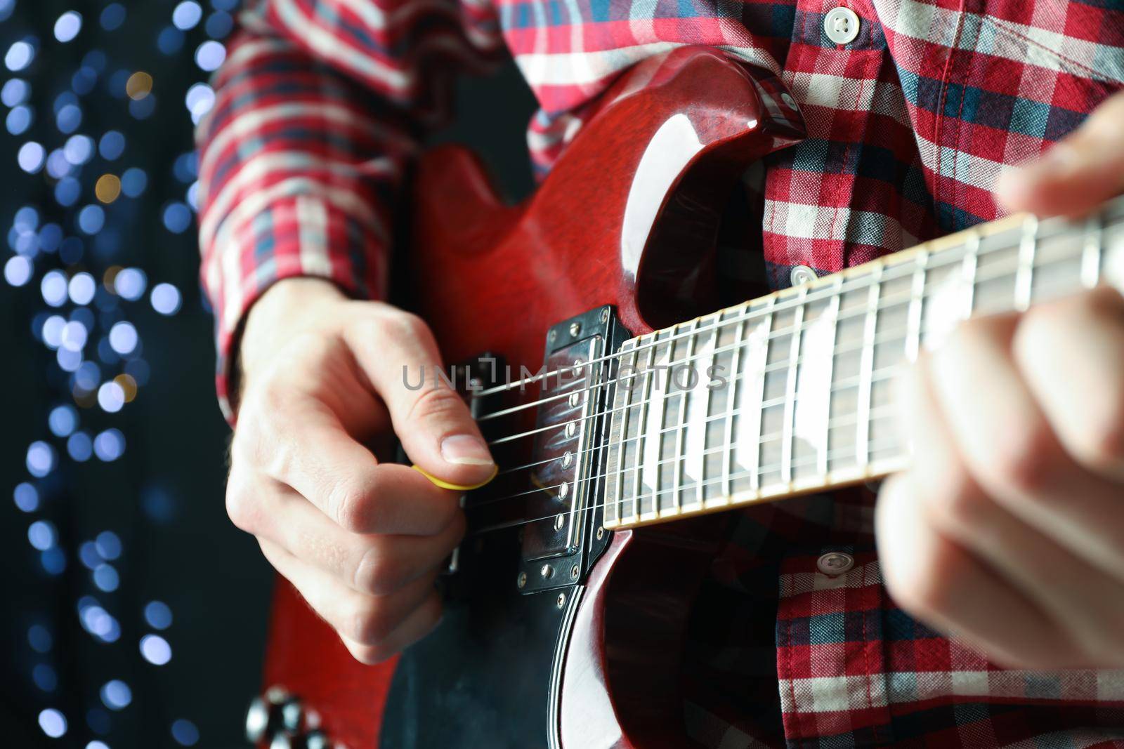 Man playing on electric guitar against dark background with blurred lights